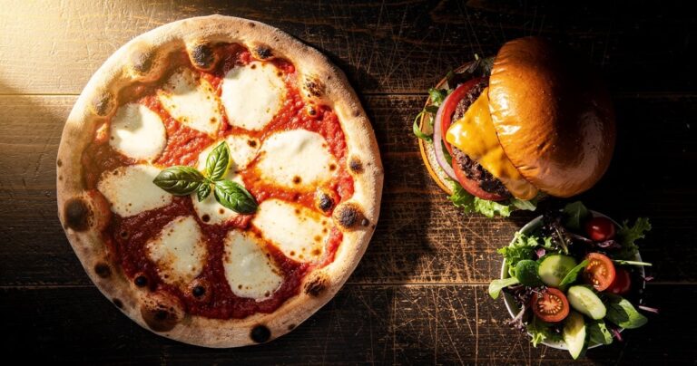 Pizza margherita et burger gourmet côte à côte sur une table en bois